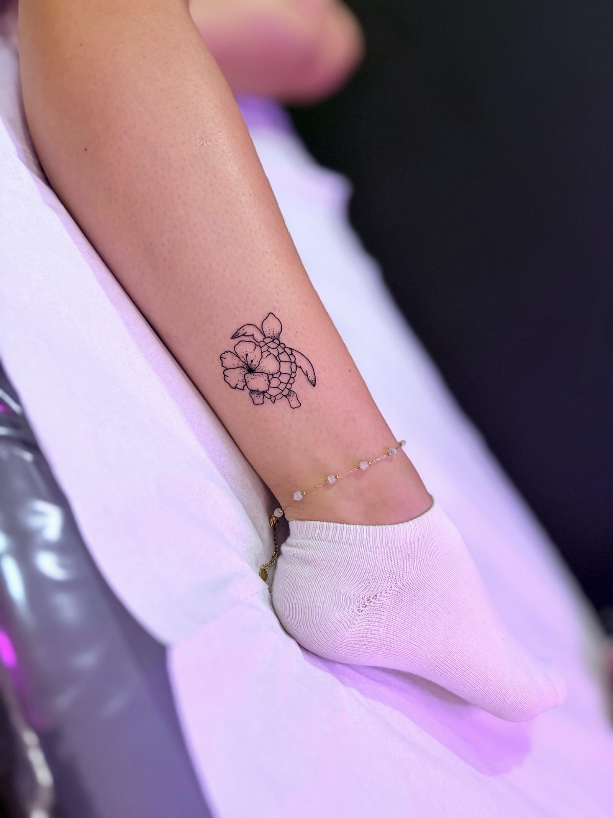 Sea turtle tattoo with a flower on the ankle of a person.