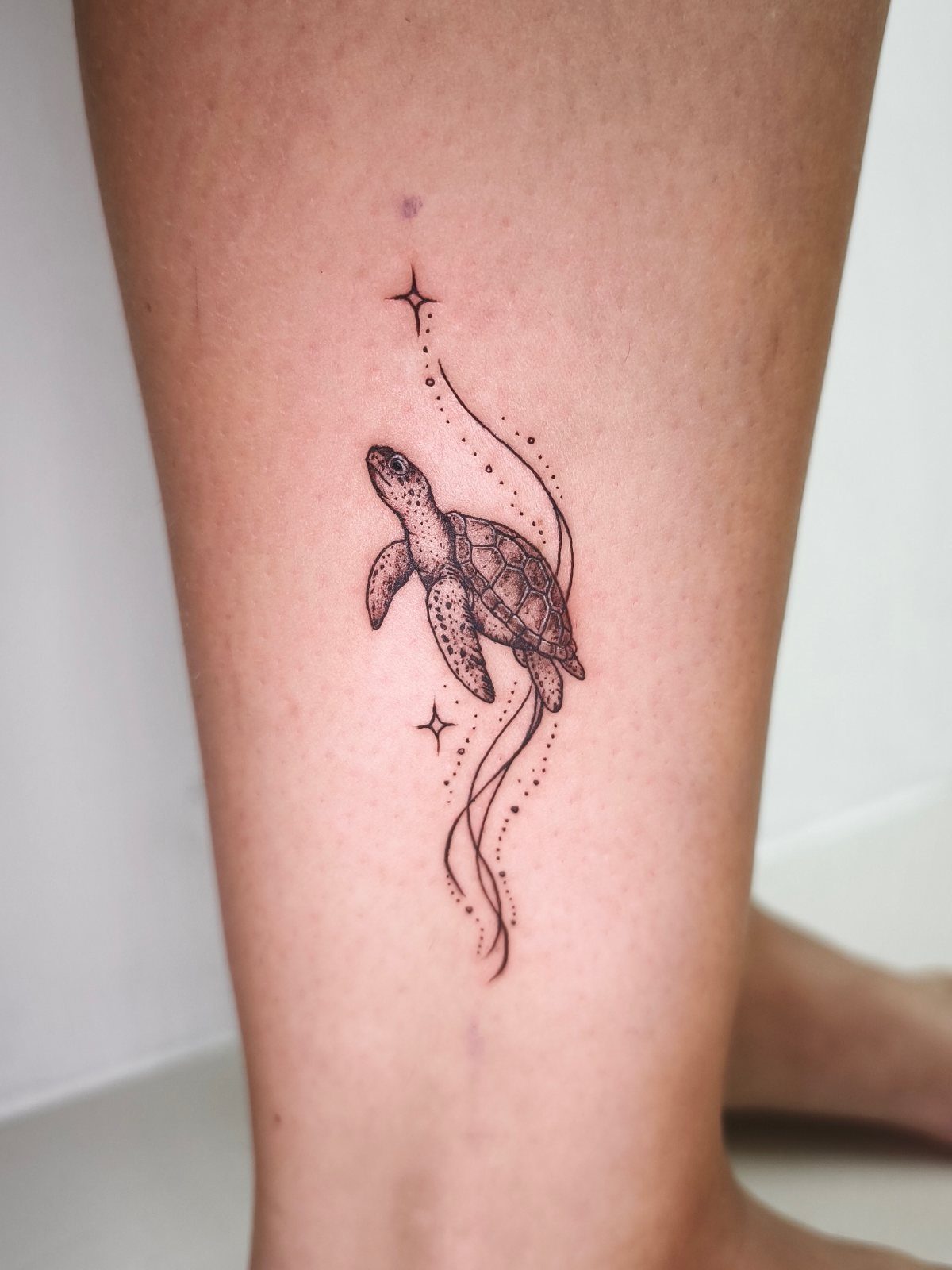 Sea turtle tattoo on an ankle with delicate lines and small stars.