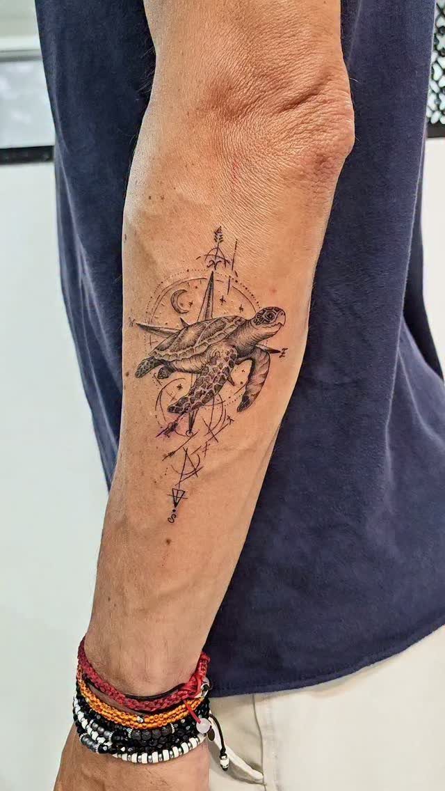 Sea turtle tattoo on a forearm with geometric lines and compass details.