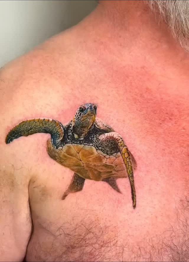 Realistic sea turtle tattoo with detailed coloring on a person's upper chest.