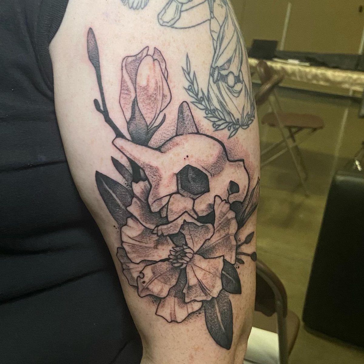 Black and grey tattoo of a skull surrounded by blooming flowers on an arm