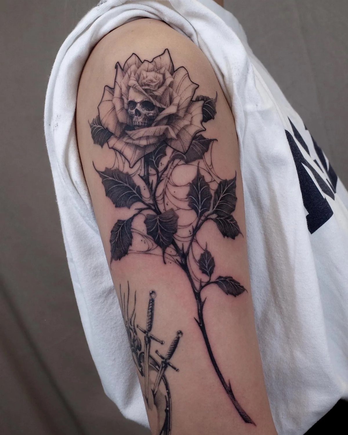 Black ink tattoo of a skull inside a rose with a spiderweb on arm