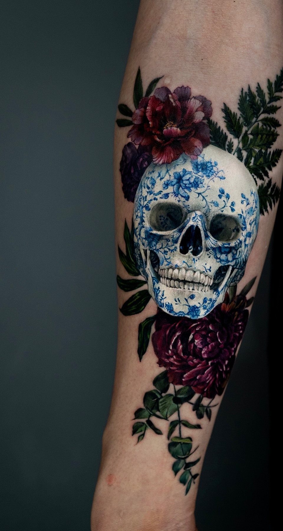 Porcelain patterned skull tattoo surrounded by red peonies and green fern leaves
