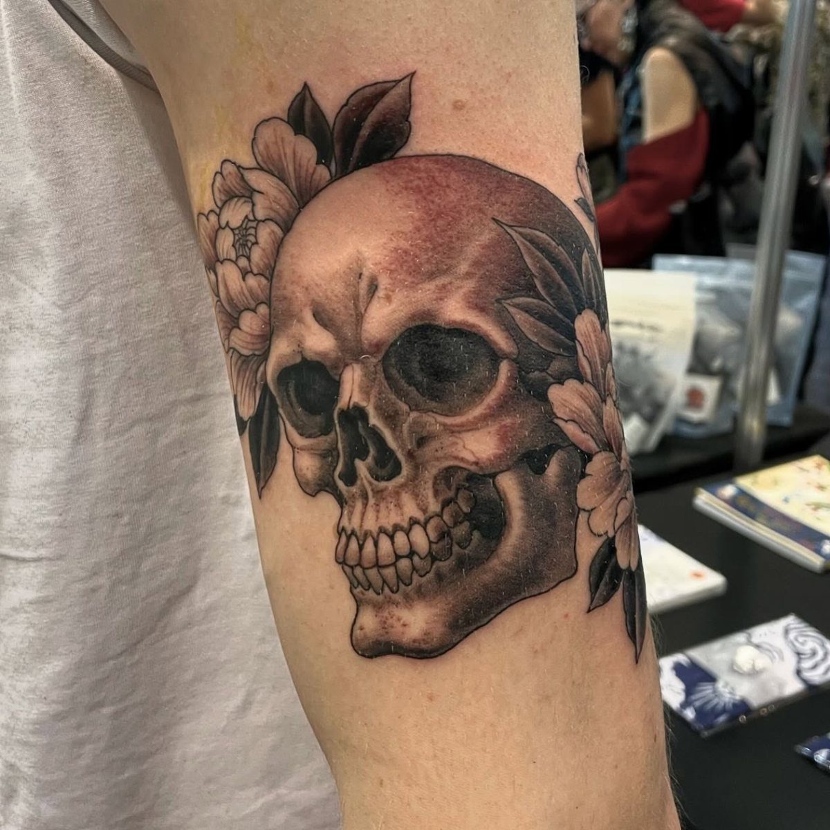 Skull tattoo on an arm framed by large flowers and dark leaves