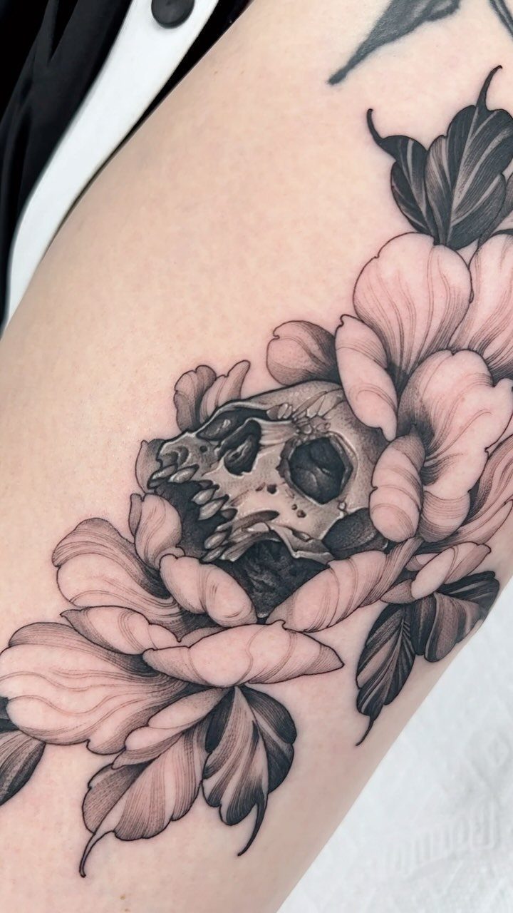 Skull partially surrounded by flowing peony flowers and leaves in black and grey ink.