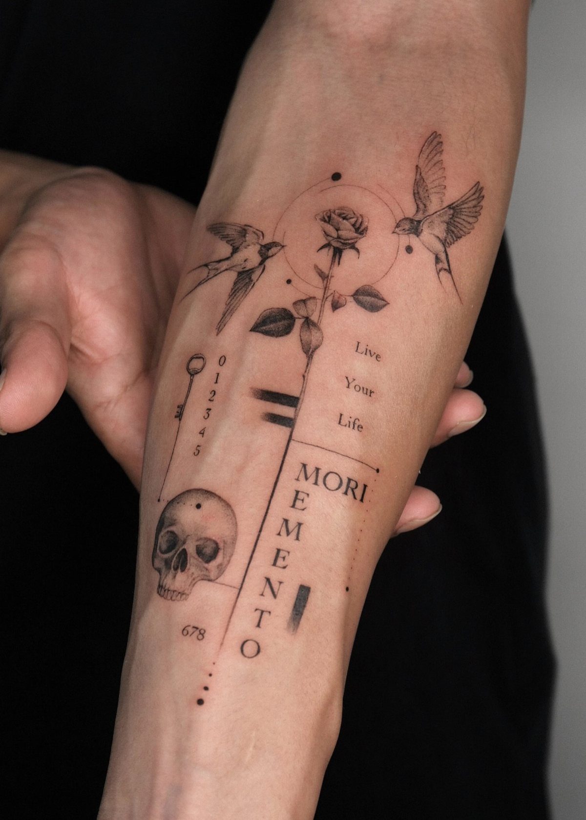Forearm tattoo with a skull, rose, birds, and geometric lines with Memento Mori text
