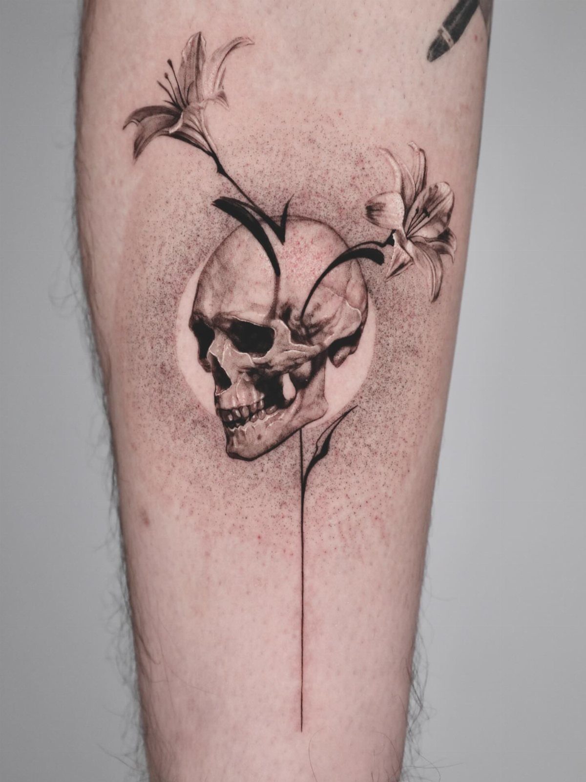 Black and grey tattoo of a skull with lily stems growing through it