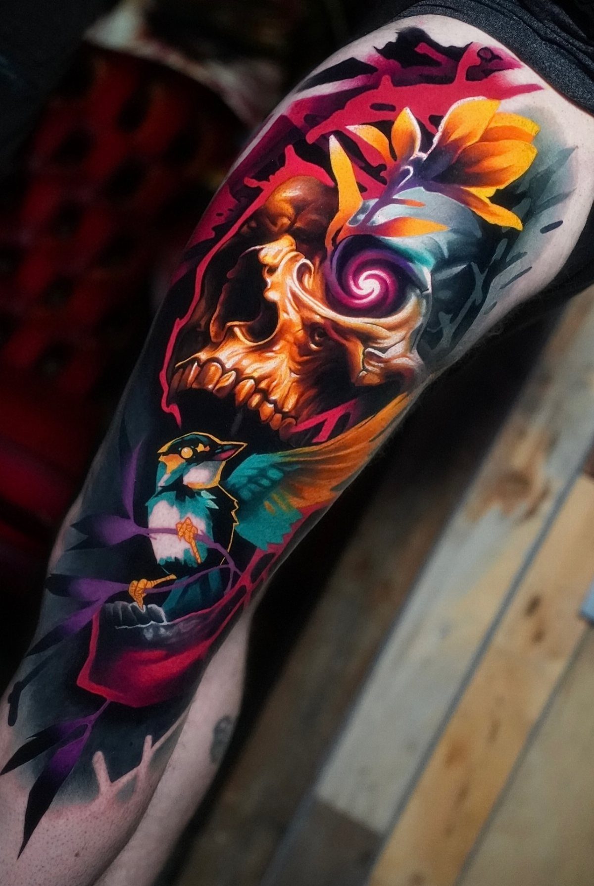 Colorful tattoo of a skull with orange flowers and a small bird on skin