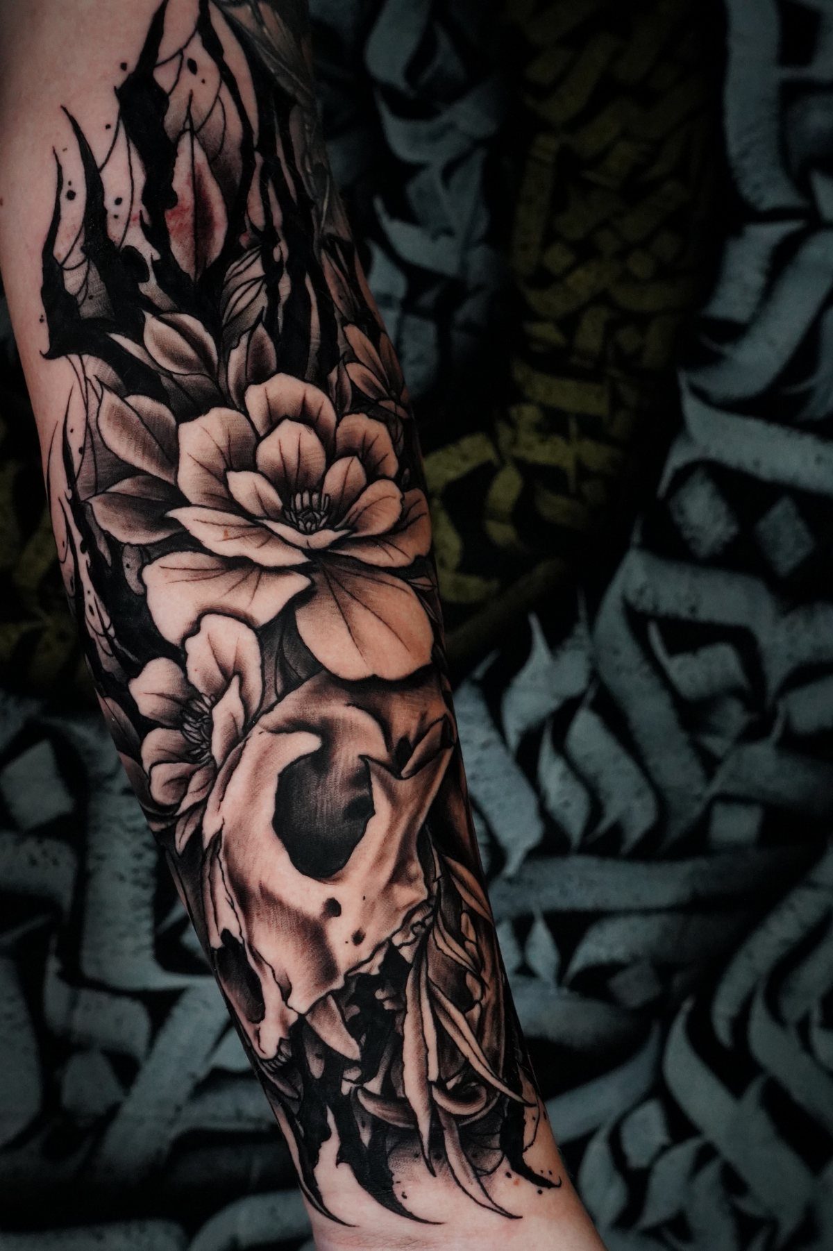 Black and grey tattoo of a skull with large magnolia flowers and foliage.