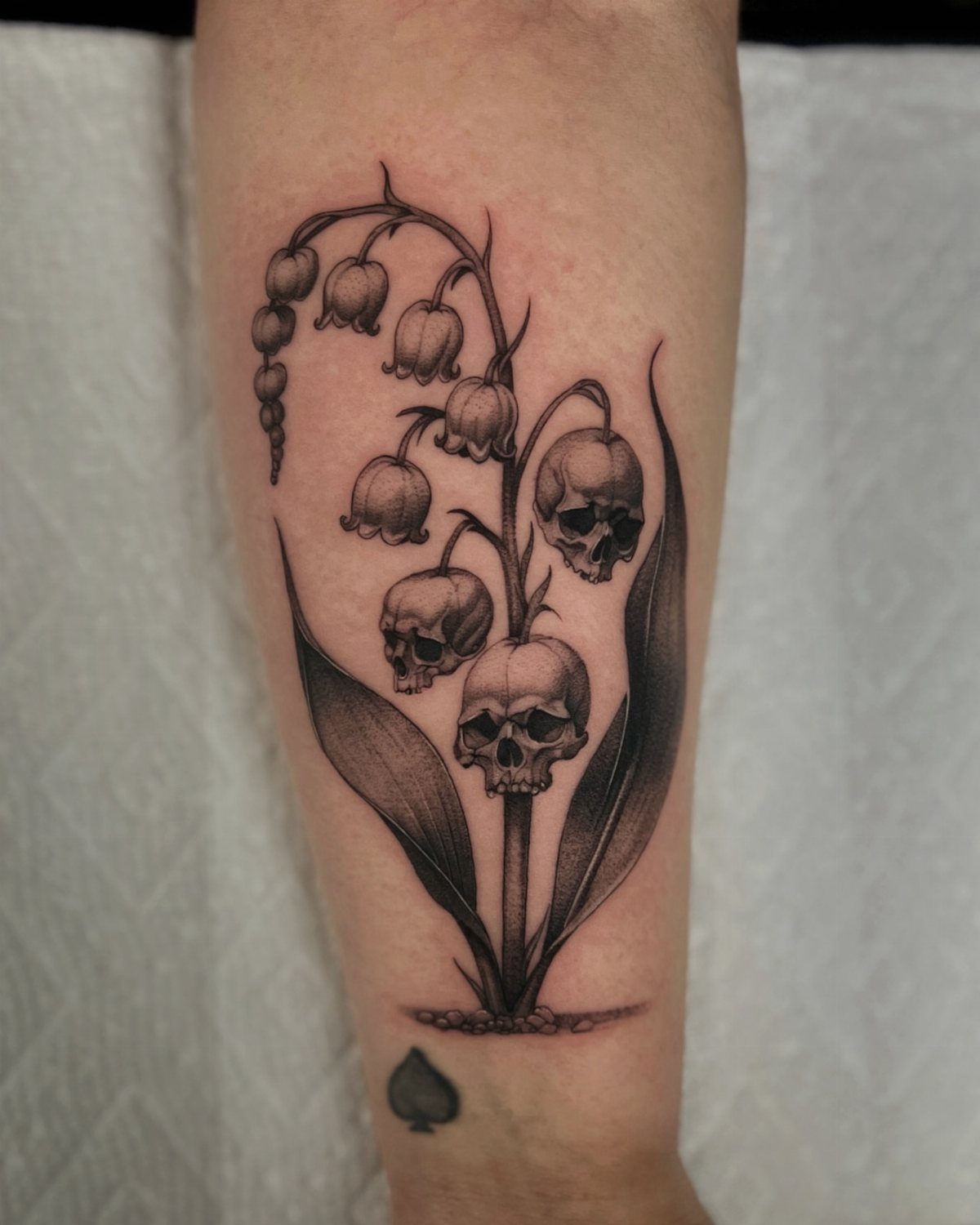 Lily of the valley tattoo with small human skulls replacing some flower bells