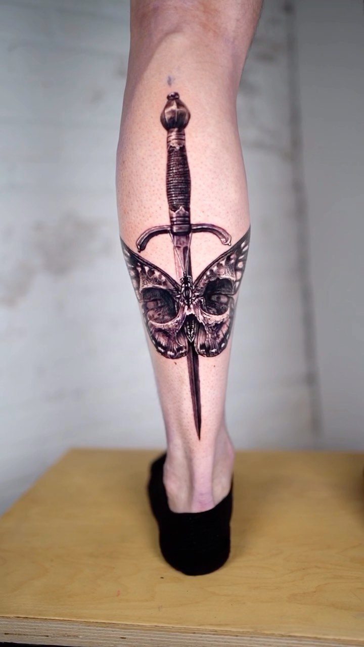 Tattoo on a lower leg showing a dagger piercing a winged skull.