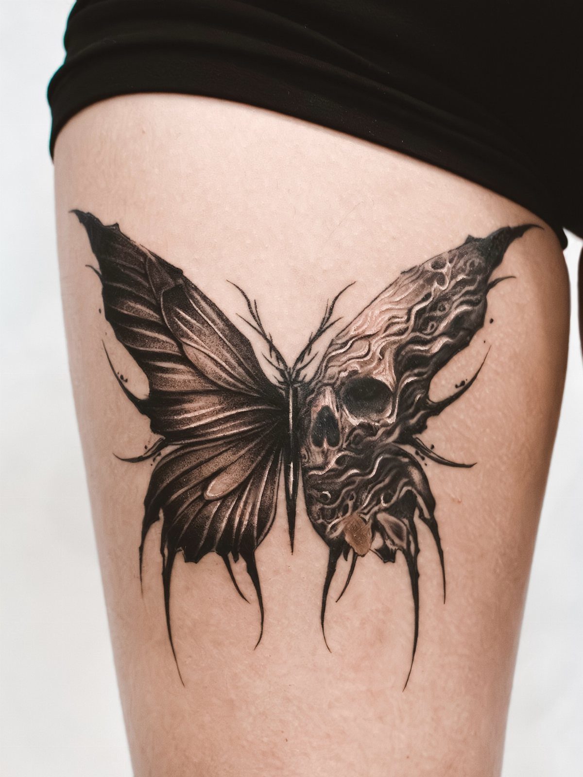 Butterfly skull tattoo on a thigh with a dark gothic aesthetic.