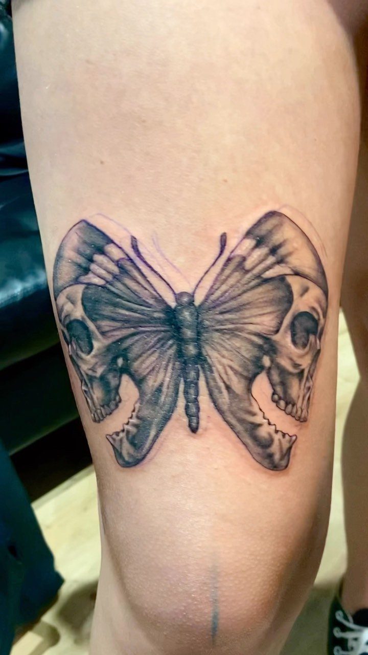 Butterfly tattoo with skull halves as wings on a person's leg