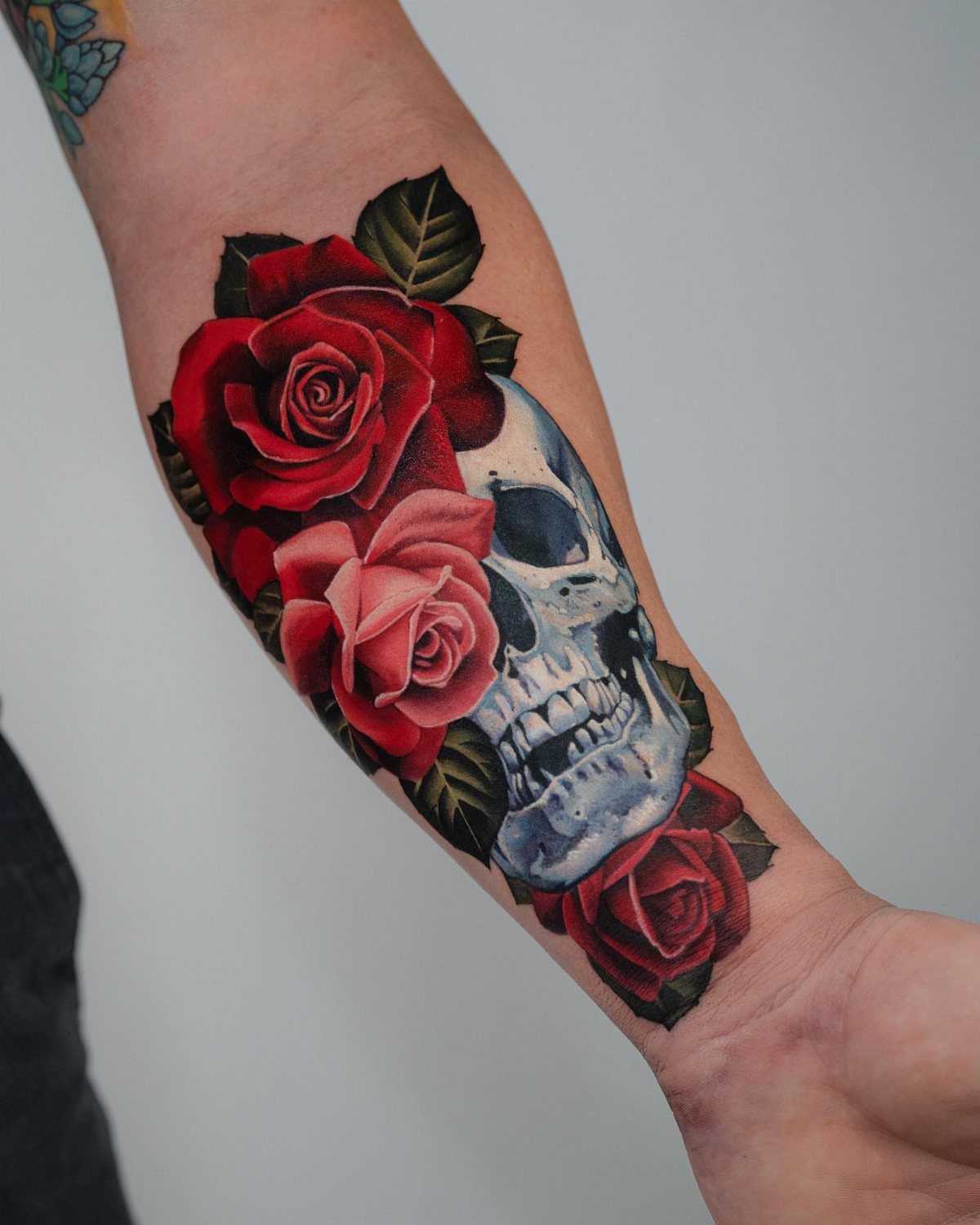 Realistic skull tattoo with vibrant red and pink roses on a person's forearm