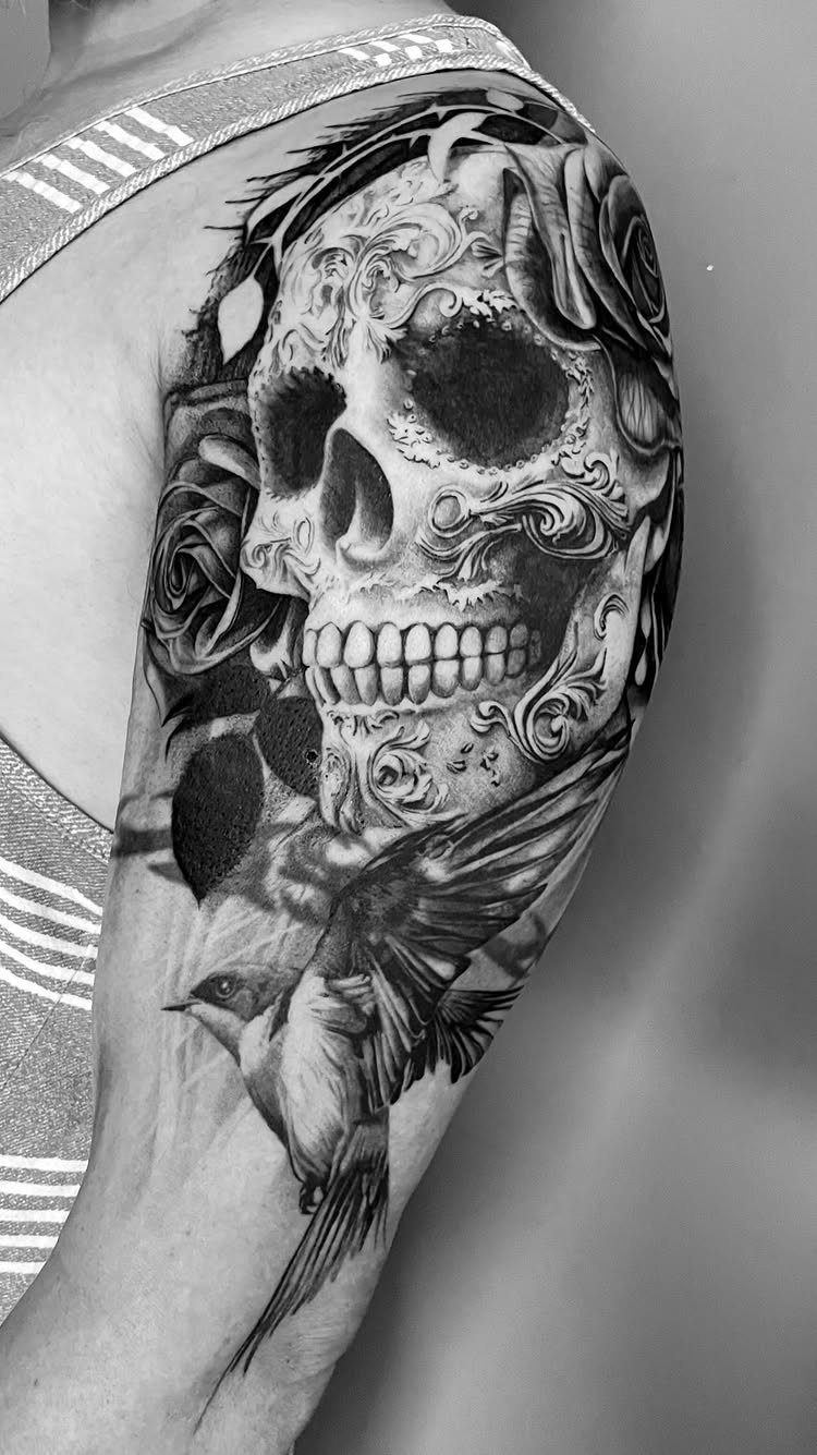 Sugar skull tattoo with roses and a bird on a person's upper arm.