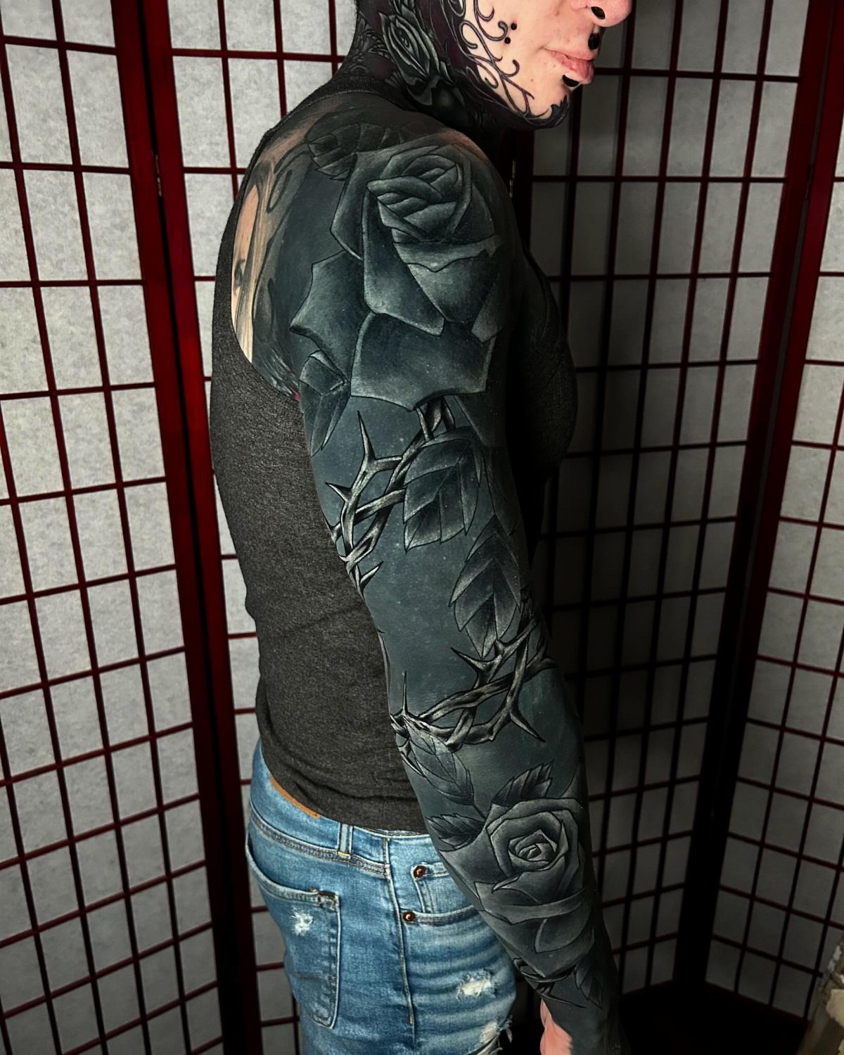 Black rose bush sleeve tattoo covering a person's entire arm with thorny stems.