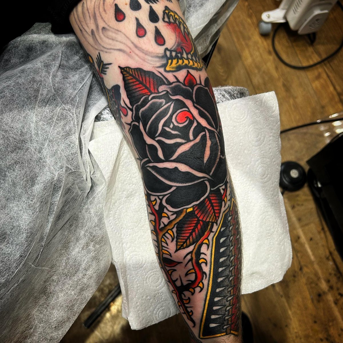 Bold black rose tattoo with red details on a person's forearm