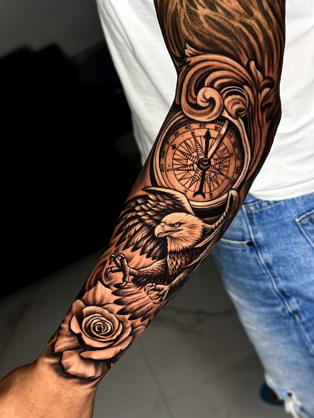 Tattoo on an arm featuring a compass, an eagle, and a black rose.