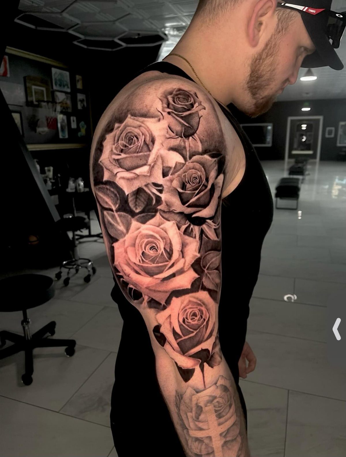 Realistic black and grey rose sleeve tattoo on a man's upper arm.