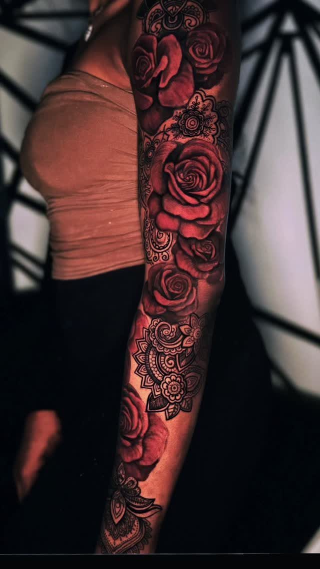 Full sleeve tattoo of red roses and mandalas on a person's arm.