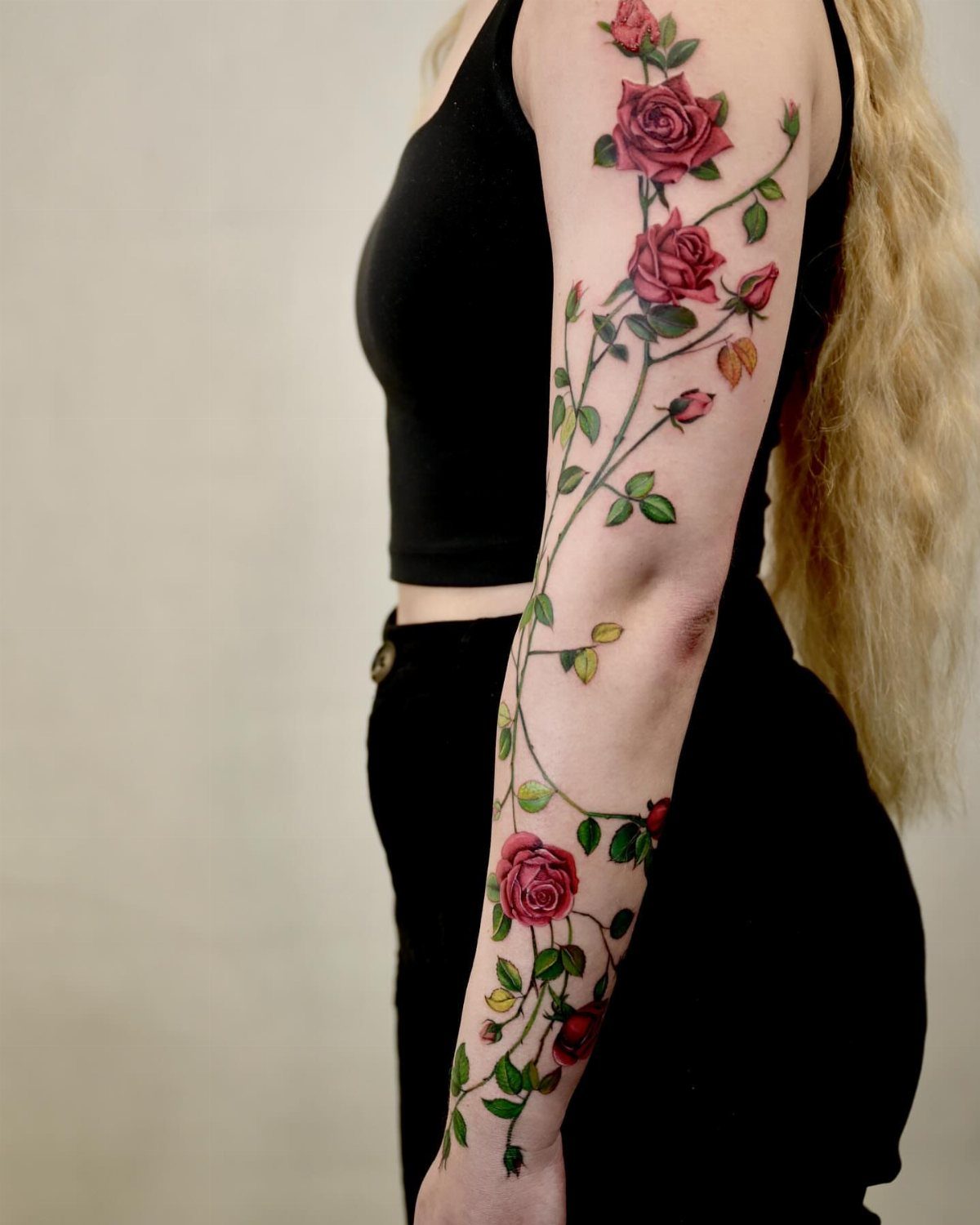 Full-sleeve tattoo of a red rose bush with green leaves on an arm