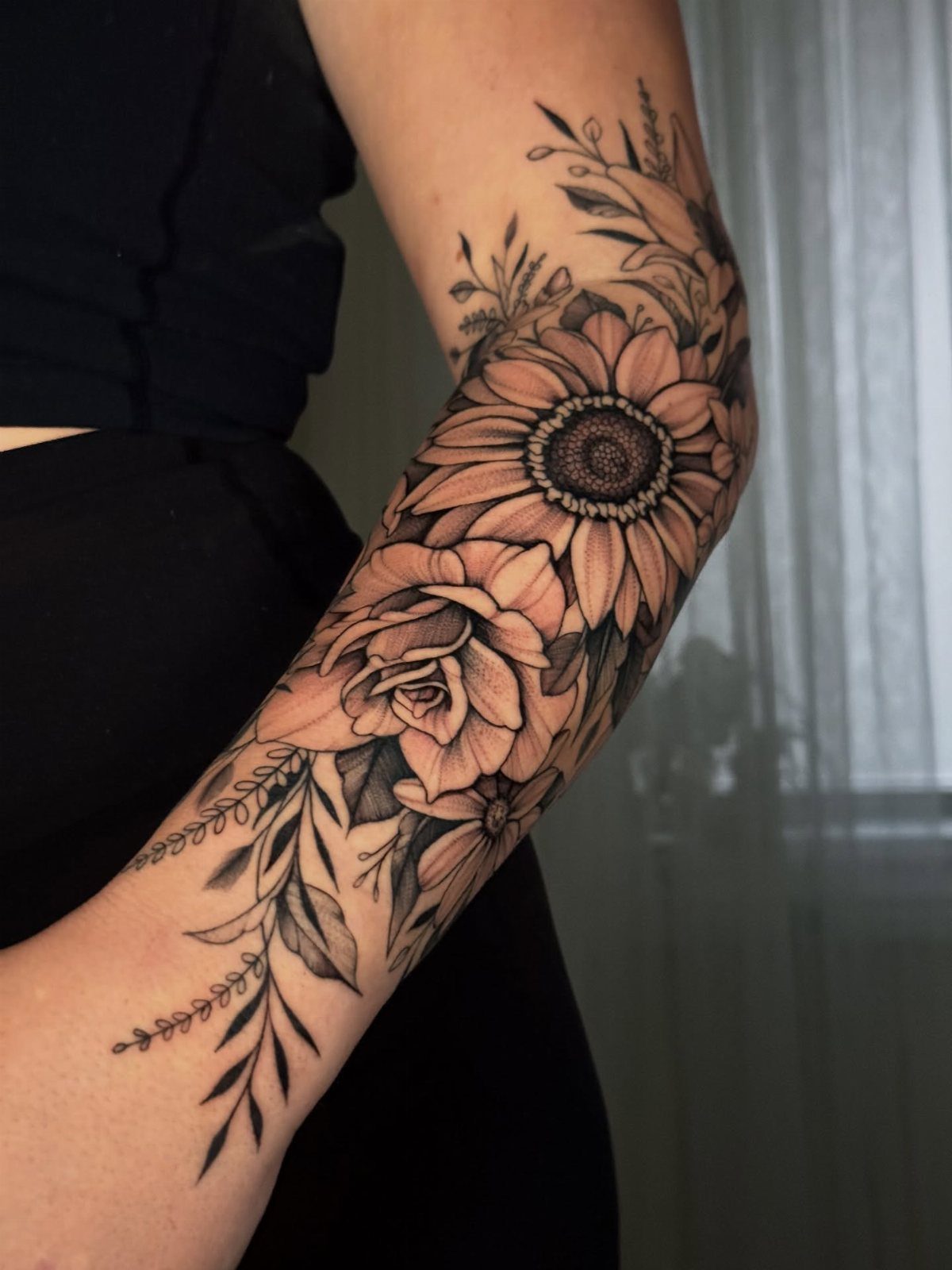 Black and grey tattoo of a sunflower and rose on a person's arm.