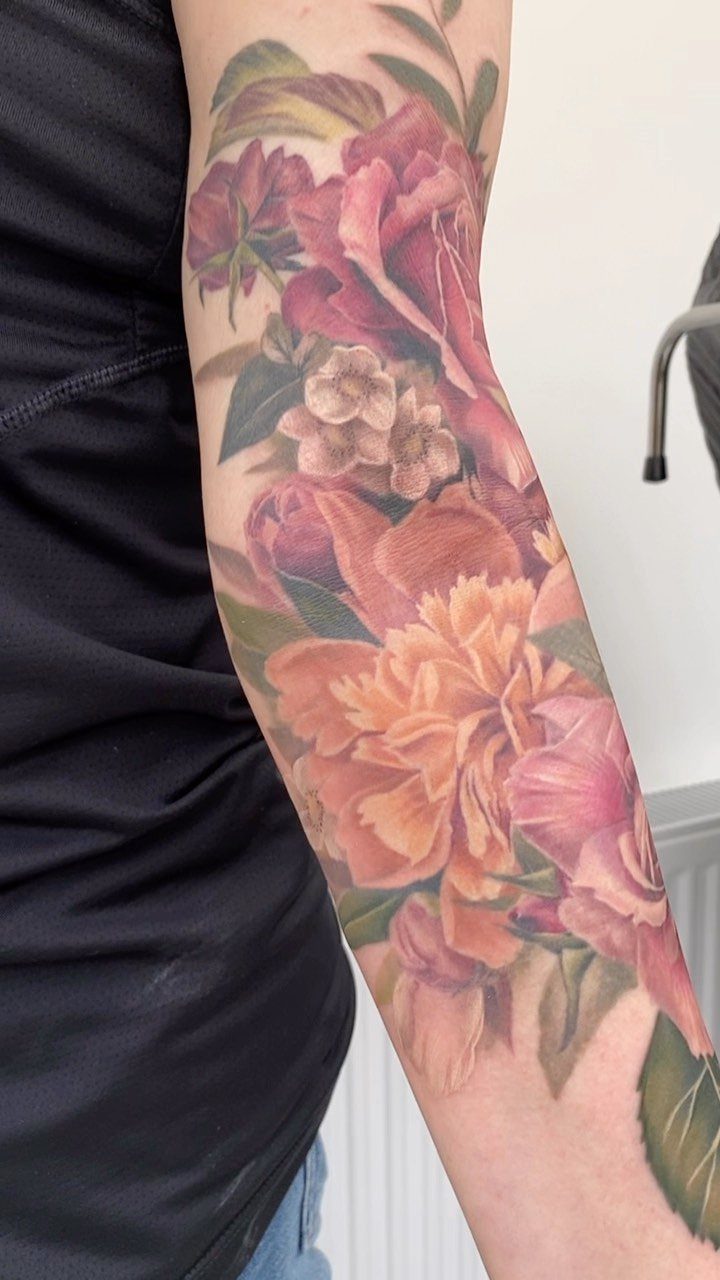 Colorful rose and peony sleeve tattoo on a person's arm with soft shading.