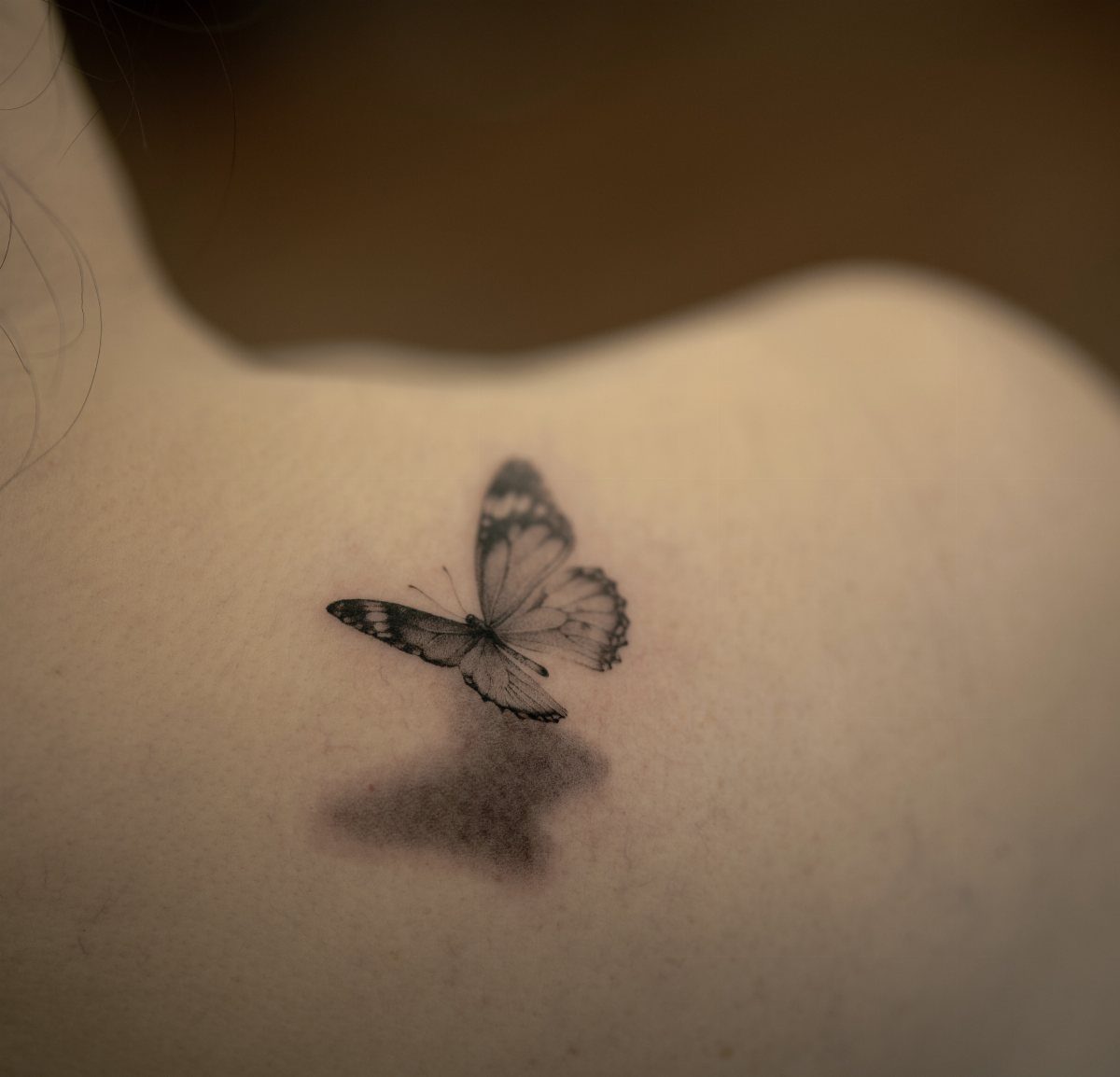 Realistic black and grey butterfly tattoo on a shoulder with a 3D shadow.
