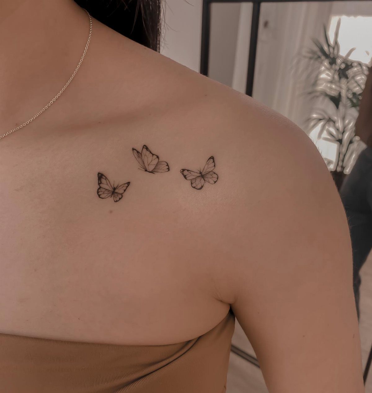 Three small black butterfly tattoos scattered across a person's shoulder and collarbone.