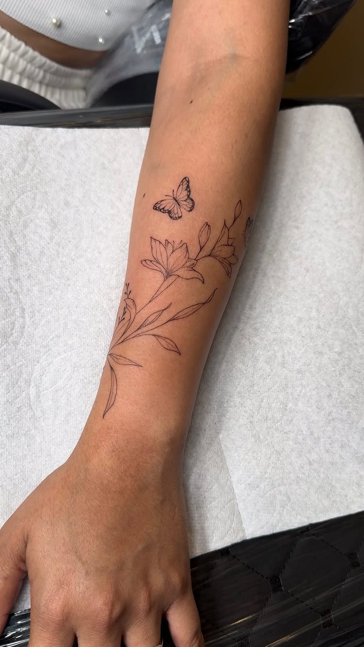 Fine-line tattoo of a small butterfly and lilies on a person's forearm