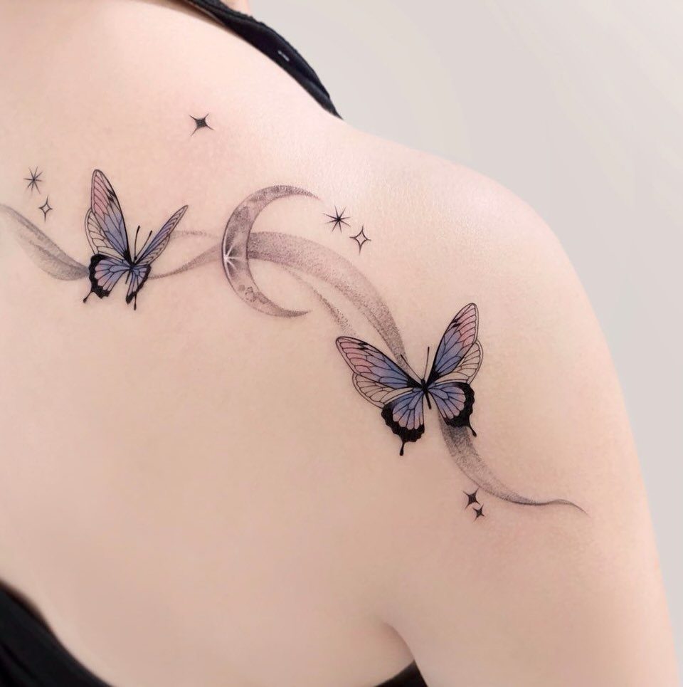 Two blue butterflies and a crescent moon tattoo with stars on a shoulder
