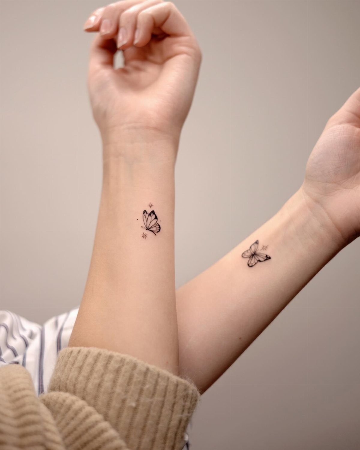 Two small black ink butterfly tattoos on the inner wrists of two people.