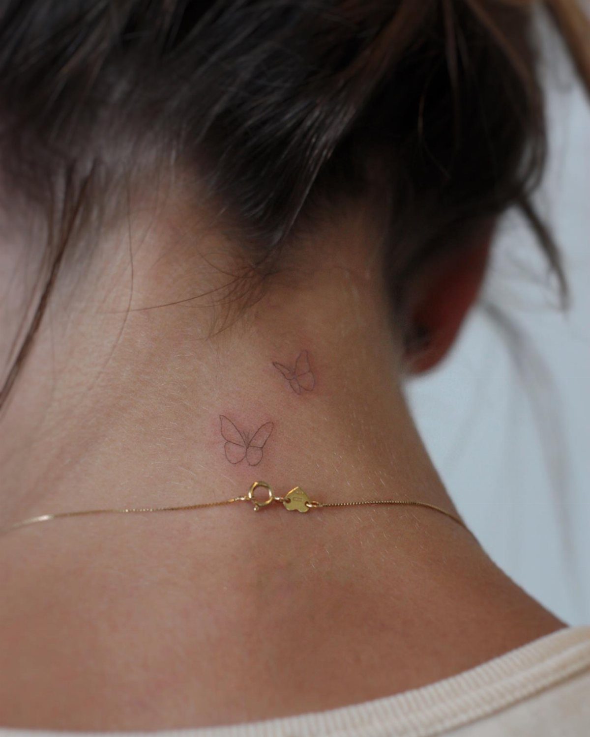 Two small minimalist butterfly tattoos on the back of a person's neck.