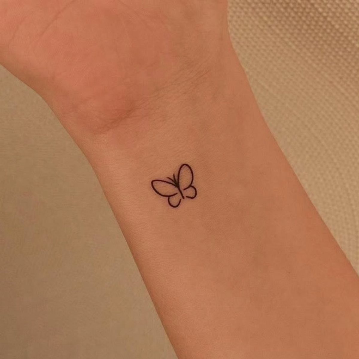 Small black linework butterfly tattoo on a person's inner wrist.