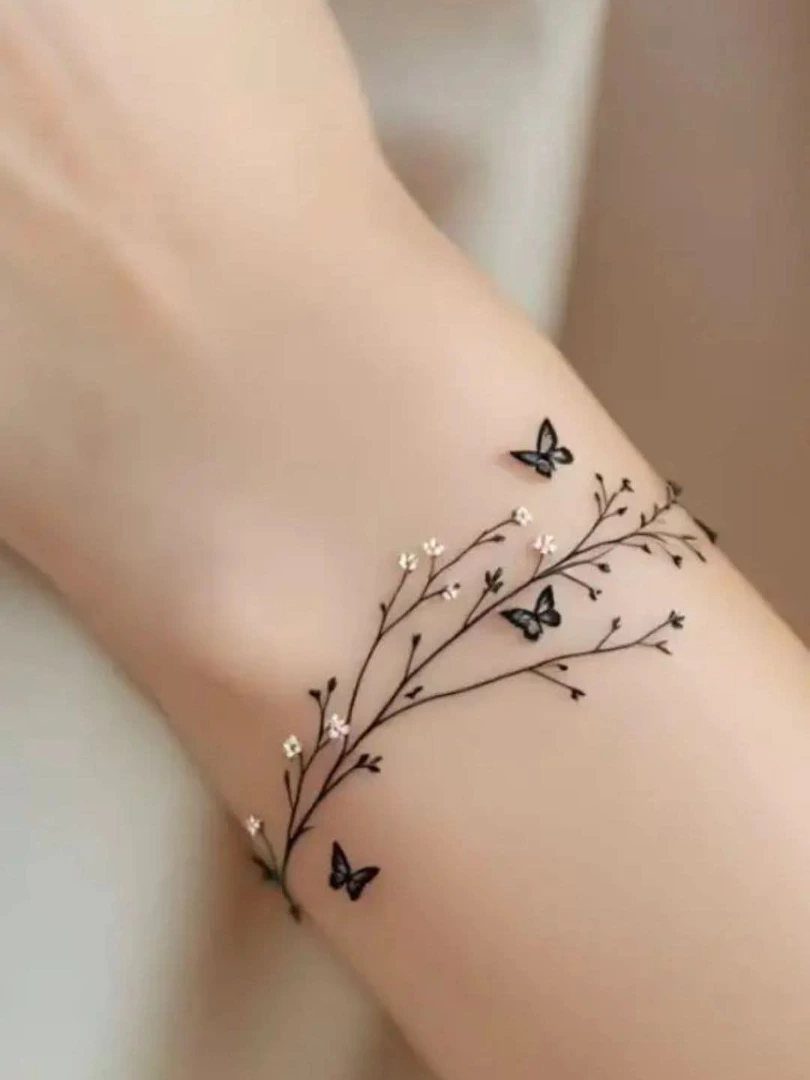 Small black butterfly tattoos on a wrist with delicate flowering vine branches.