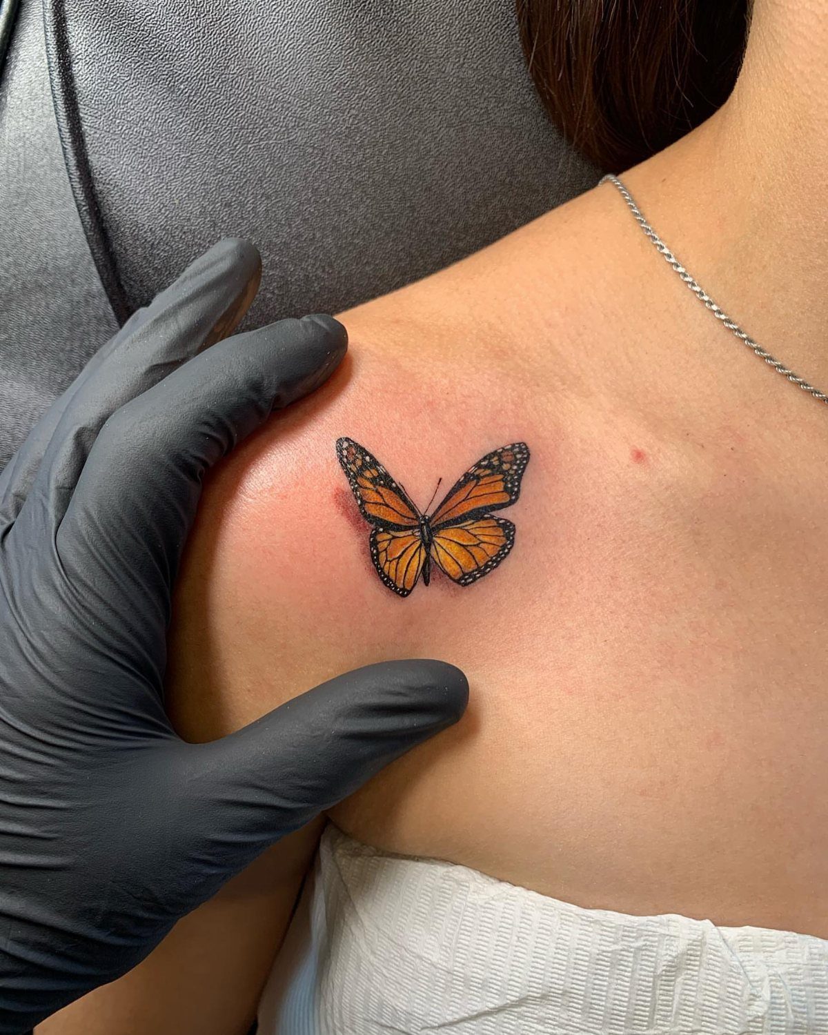 Vibrant orange monarch butterfly tattoo on a person's shoulder next to gloved hand