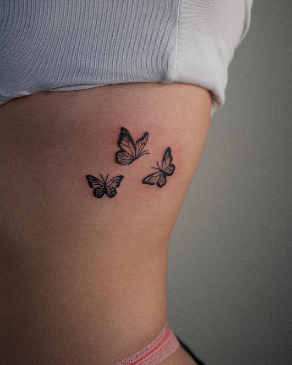 Three small black butterfly tattoos on a person's side torso near the waist