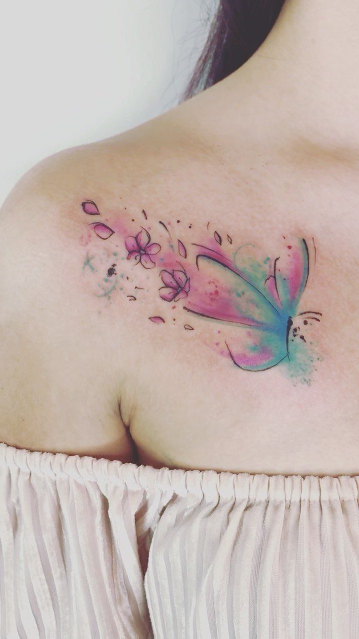 Watercolor butterfly tattoo with pink flowers and colorful splatters on a shoulder