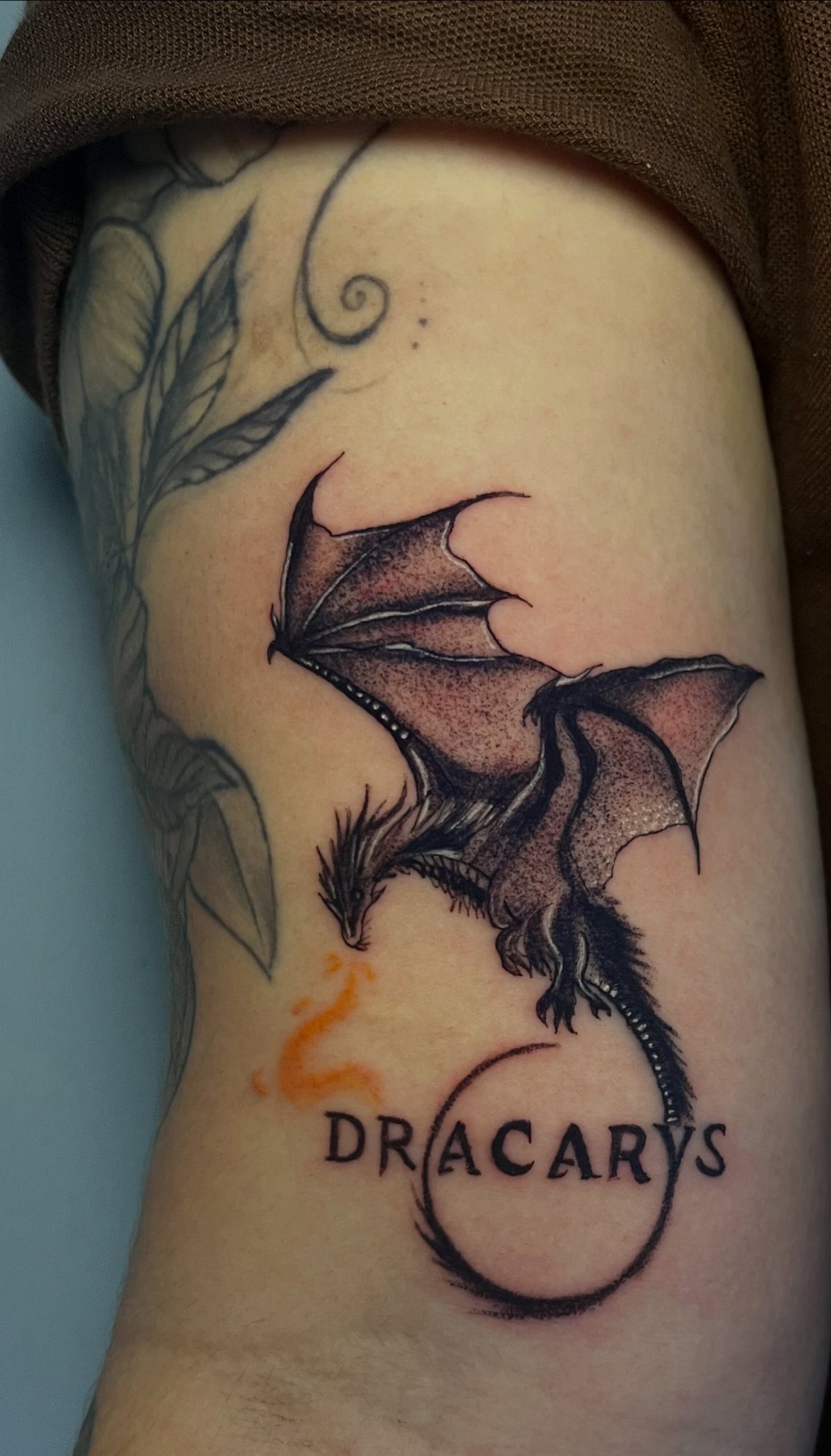 Detailed black ink dragon tattoo with the word Dracarys on a person's arm.