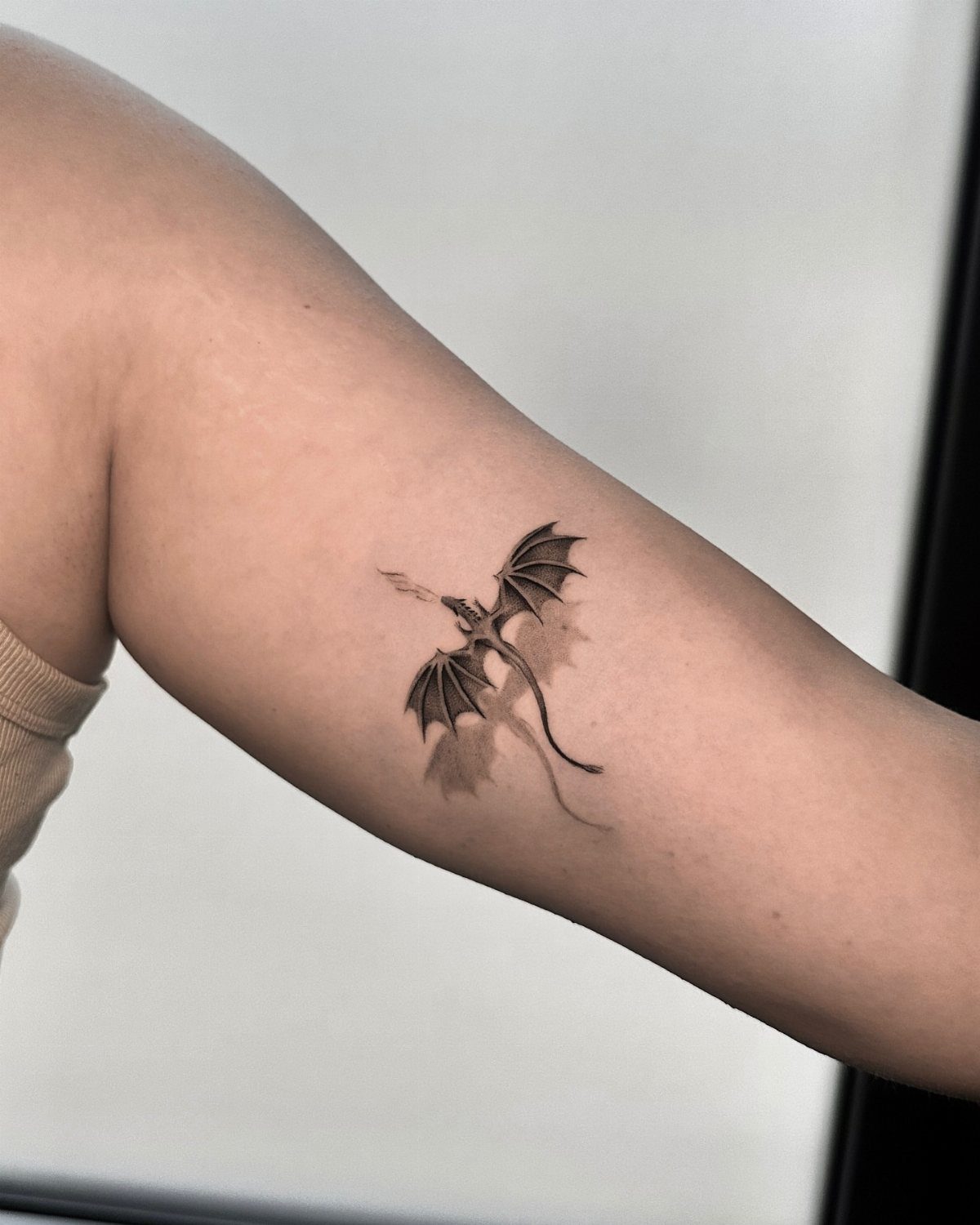 Small black ink dragon tattoo breathing fire on a person's forearm