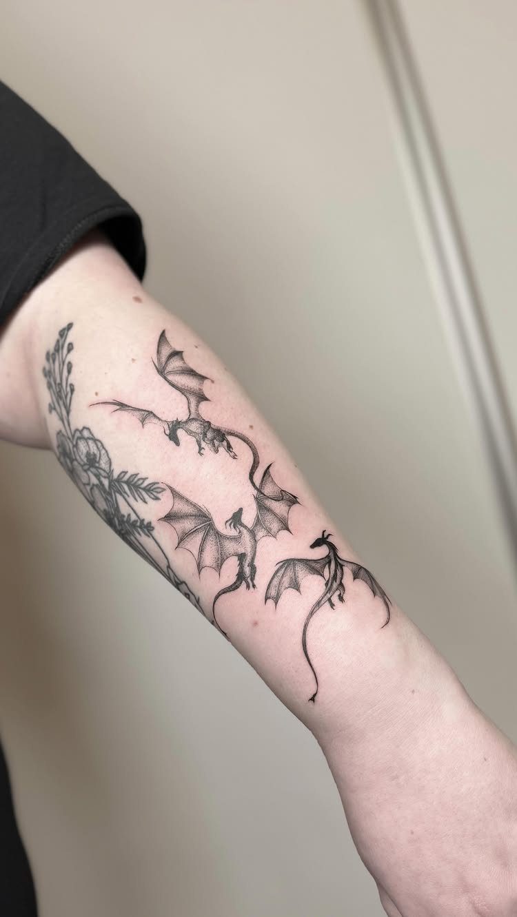 Three small black ink dragon tattoos on a person's forearm in flight.