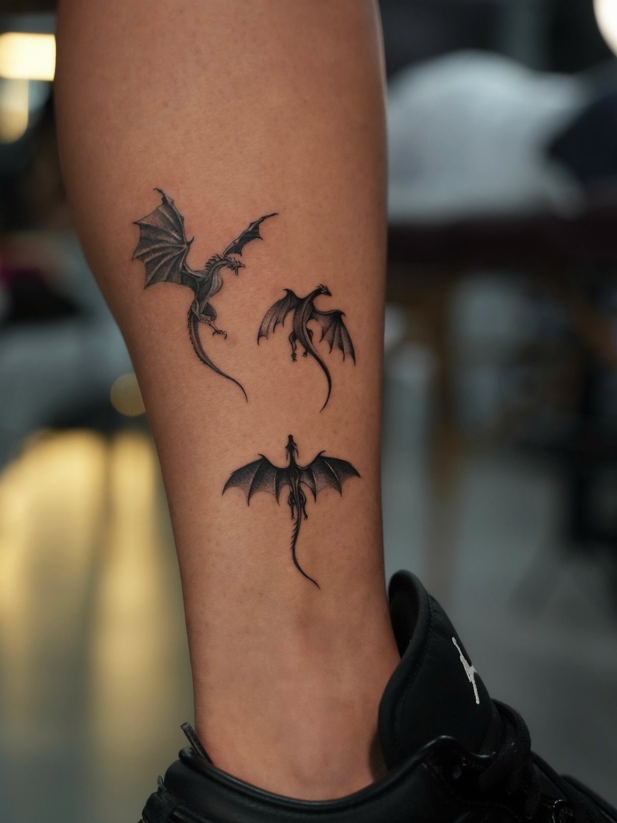 Three small black dragon tattoos on a person's ankle and lower leg.