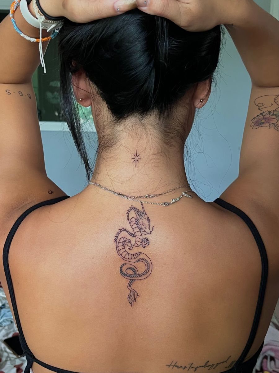 Black ink dragon tattoo centered on the upper back of a person.