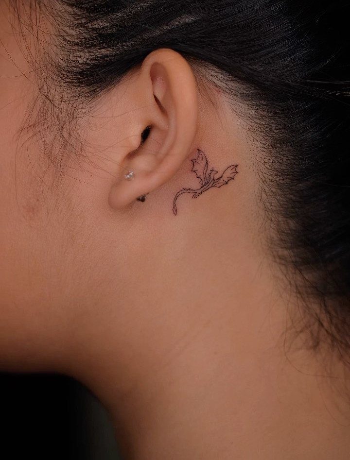 Small black dragon tattoo located on the skin behind a person's ear.