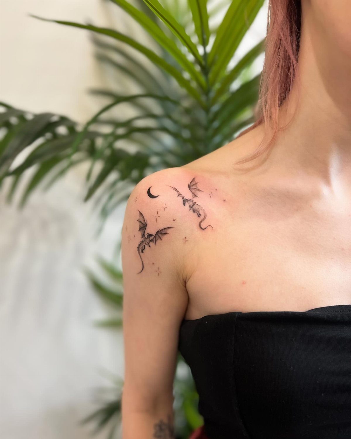 Two small minimalist dragon tattoos with a moon and stars on a shoulder