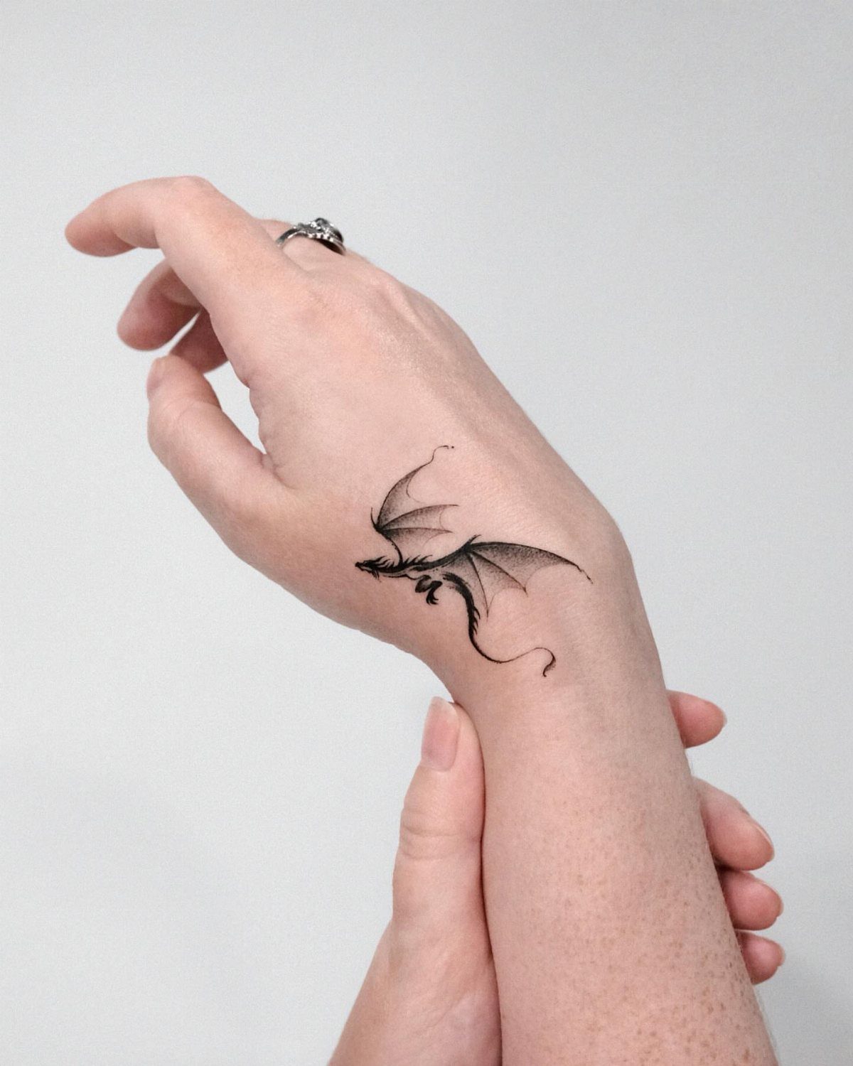 Small black dragon tattoo on a person's wrist with wings spread wide.