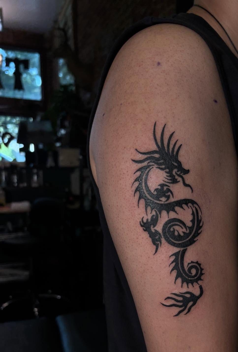 Tribal dragon tattoo with bold black lines on a person's upper arm