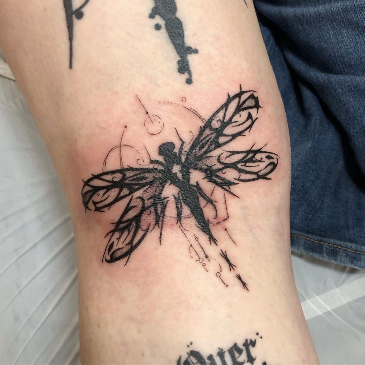 Abstract black ink dragonfly tattoo with swirling lines on a person's leg