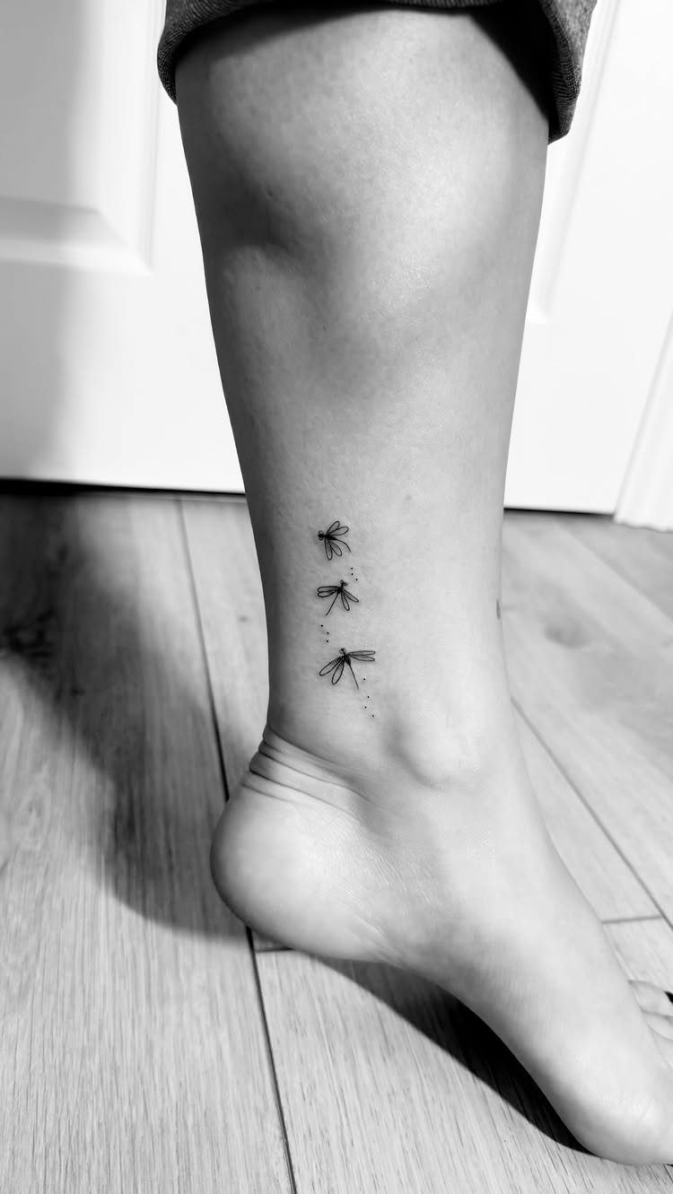 Three small dragonfly tattoos arranged vertically on a person's inner ankle.