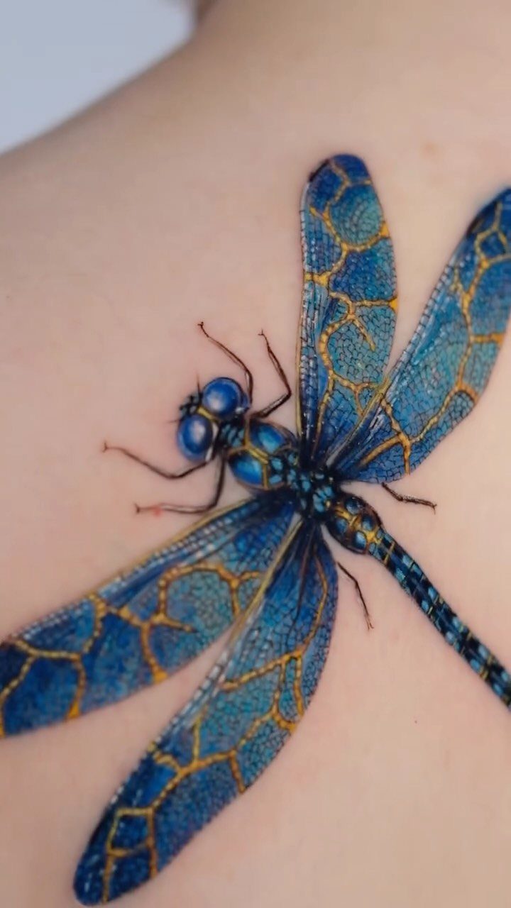 Blue dragonfly tattoo with gold wing veins on pale skin